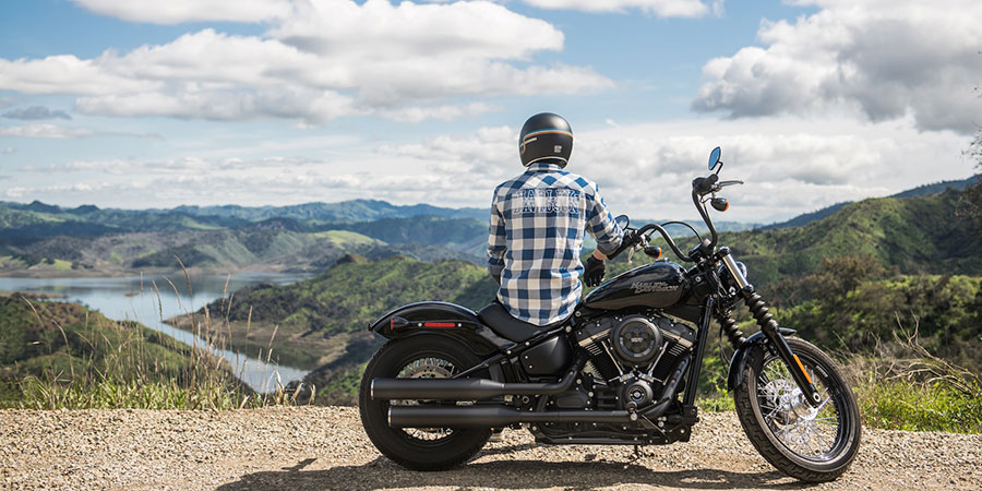 a man wearing a black helmet and checkered shirt, sitting on a Harley Davidson motorcycle while looking at the view of the lake